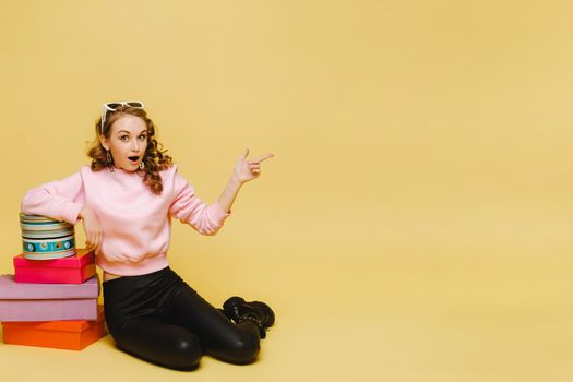 A happy young woman with colorful paper boxes after shopping isolated on an orange Studio background. Seasonal sales, purchases, spending money on gifts.