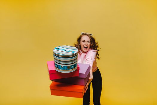 A happy young woman with colorful paper boxes after shopping isolated on an orange Studio background. Seasonal sales, purchases, spending money on gifts.