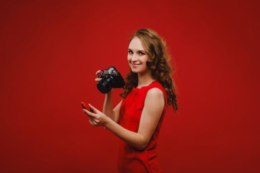 a smiling young woman with wavy hair holds a strawberry and photographs it, holding a delicious fresh strawberry on a bright red background.
