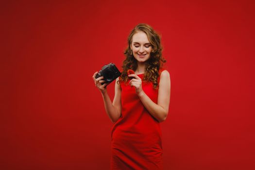 a smiling young woman with wavy hair holds a strawberry and photographs it, holding a delicious fresh strawberry on a bright red background.