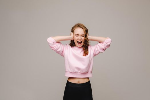 A beautiful girl on a gray background holds her head and screams emotionally.