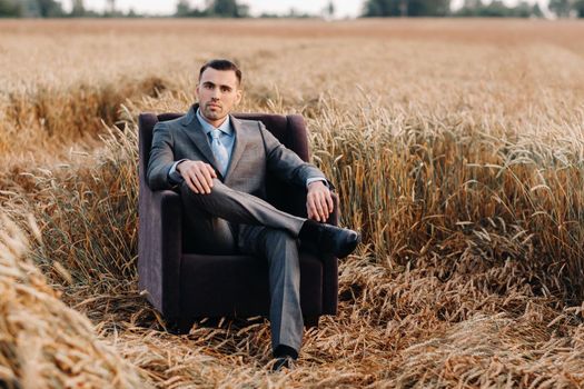 Portrait of a businessman in a gray suit and tie sitting in a chair in a wheat field.