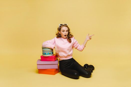 A happy young woman with colorful paper boxes after shopping isolated on an orange Studio background. Seasonal sales, purchases, spending money on gifts.