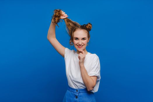 A young stylish girl pulls her hair on a blue background, a Model pulls her long hair