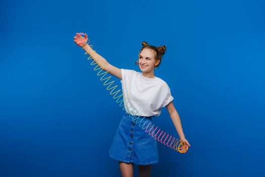 Beautiful young girl playing with a rainbow slinky, a toy of her childhood on a blue background.