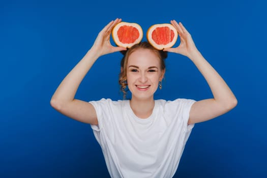 Surprised, the laughing girl holds the grapefruit like ears. Vegan lifestyle. Smiling woman , eating concept.Diet organic , weight loss and healthy food. Smoothies and fresh juice