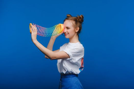 Beautiful young girl playing with a rainbow slinky, a toy of her childhood on a blue background.