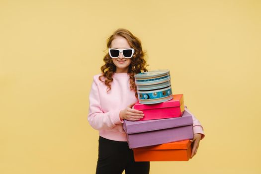 A happy young woman with colorful paper boxes after shopping isolated on an orange Studio background. Seasonal sales, purchases, spending money on gifts.