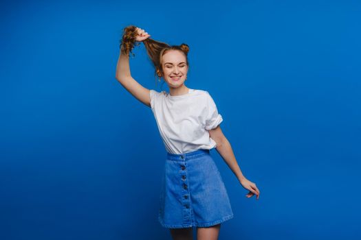 A young stylish girl pulls her hair on a blue background, a Model pulls her long hair