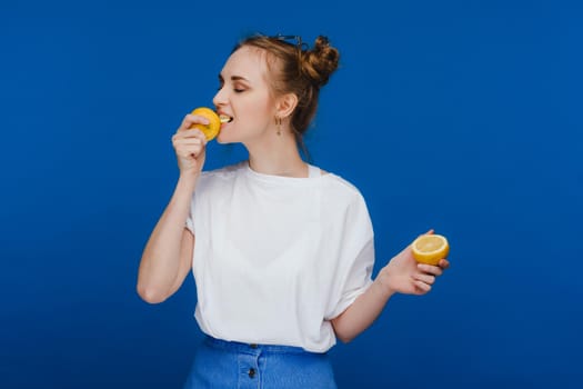 a young beautiful girl standing on a blue background holding lemons in her hand and biting