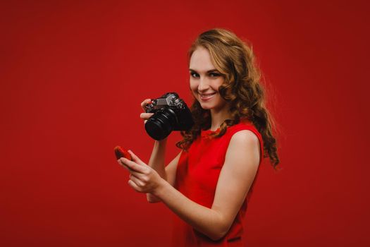 a smiling young woman with wavy hair holds a strawberry and photographs it, holding a delicious fresh strawberry on a bright red background.