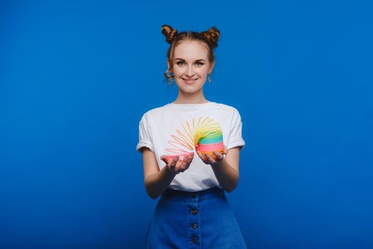 Beautiful young girl playing with a rainbow slinky, a toy of her childhood on a blue background.