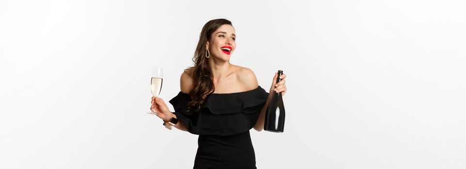 Celebration and party concept. Stylish brunette woman in glamour dress holding bottle and glass of champagne, having fun on new year holiday.