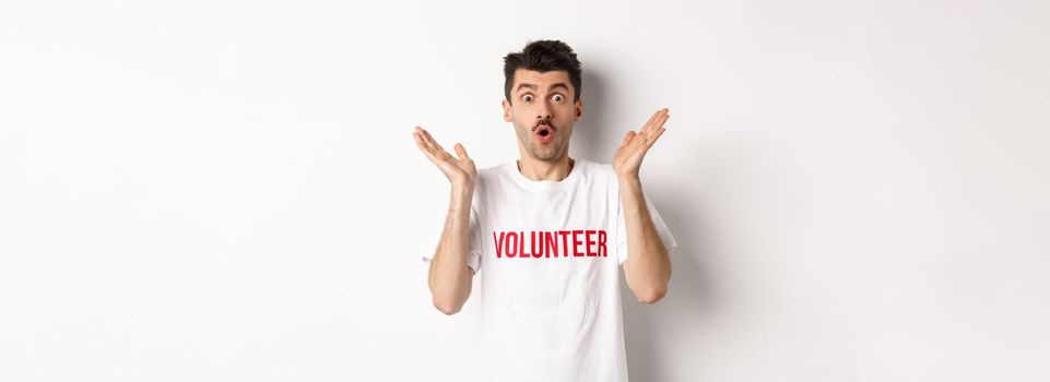 Amazed male volunteer in white t-shirt hear great news, clap hands and staring at camera surprised, posing over studio background.