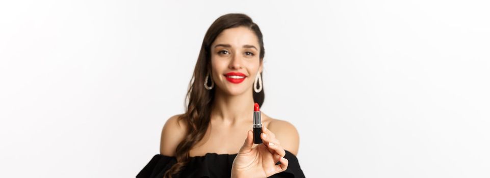 Fashion and beauty concept. Beautiful woman in black dress showing red lipstick and smiling, standing over white background.