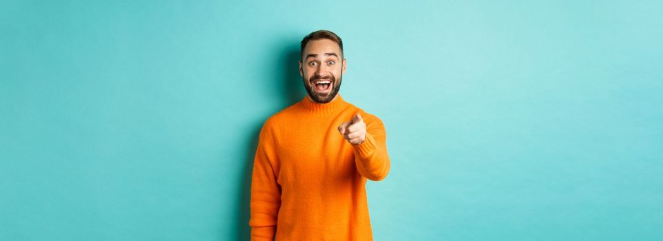 Surprised man stare happy and pointing at camera, recognize someone, excited about seeing something, standing over light blue background.