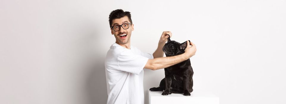 Happy young man looking at camera, showing cute dog ears and feeling rejoice, adopting a pet, standing over white background.