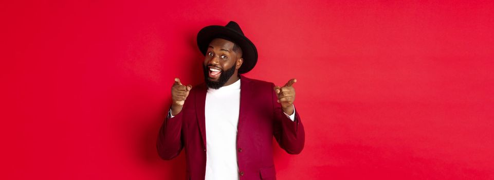 Christmas and people concept. Happy Black man celebrating New Year and dancing, wearing party outfit, red background.