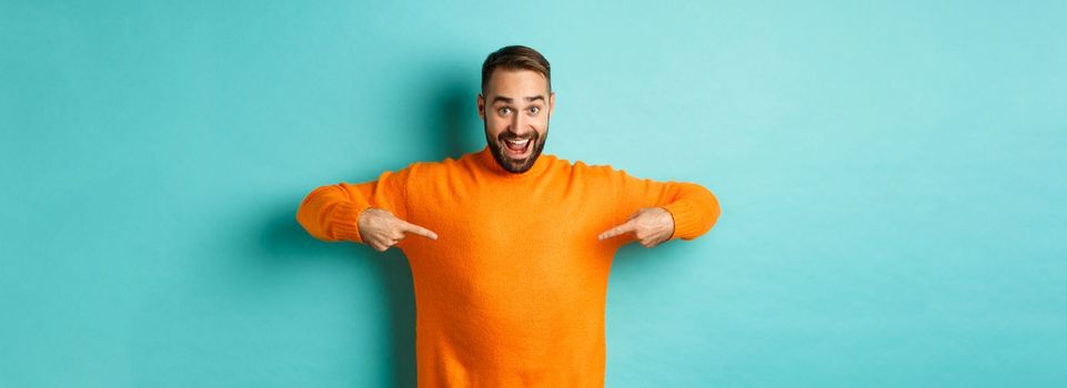 Happy man pointing at sweater, showing your logo banner on clothes, standing over light blue background.