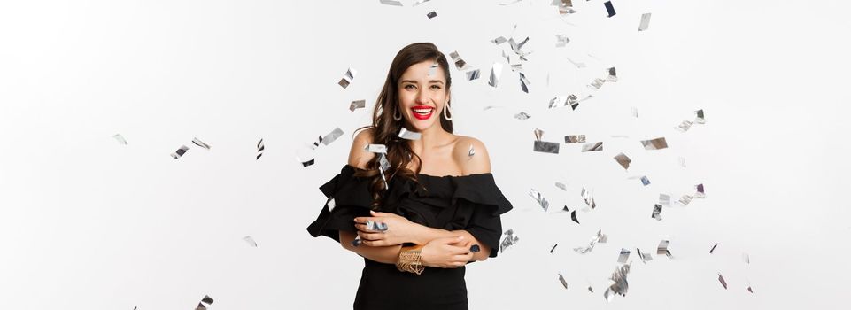 Happy woman celebrating winter holidays, smiling cheerful, partying on New Year with confetti, standing over white background.