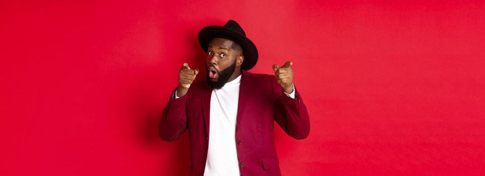 Christmas and people concept. Happy Black man celebrating New Year and dancing, wearing party outfit, red background.