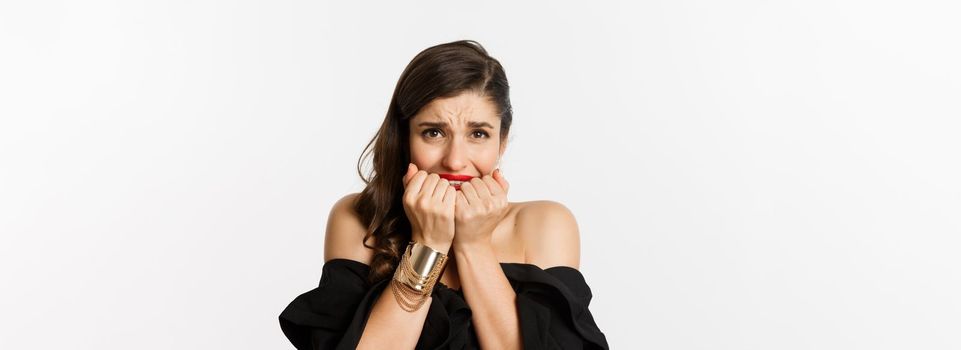 Fashion and beauty concept. Nervous woman looking concerned, biting fingernails and standing over white background.