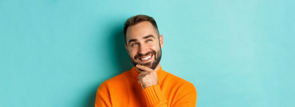 Close-up of caucasian male model having an idea, smiling and looking upper left corner thoughtful, imaging plan, standing over light blue background.