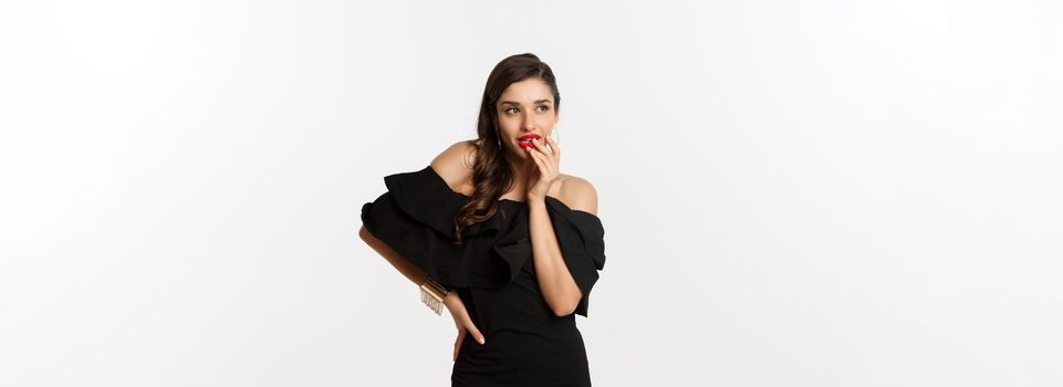 Fashion and beauty. Glamour woman in black dress thinking, having an idea, standing over white background.