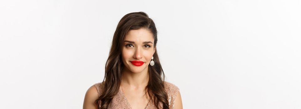 Close-up of attractive woman with hairstyle and red lips, standing in elegant dress and smiling, celebrating Christmas party, standing over white background.