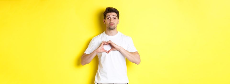 Cute guy pucker lips and waiting for kiss, showing heart gesture. Concept of love and romance.