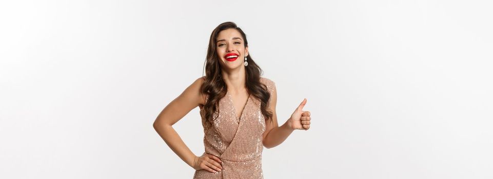 Concept of celebration, holidays and party. Happy elegant woman in evening dress with red lips, showing thumb up and laughing, approve and like something good.