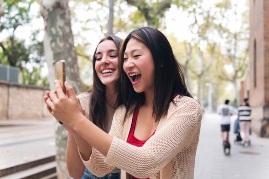 two young women having fun looking at content on a mobile phone, concept of technology of communication and social media