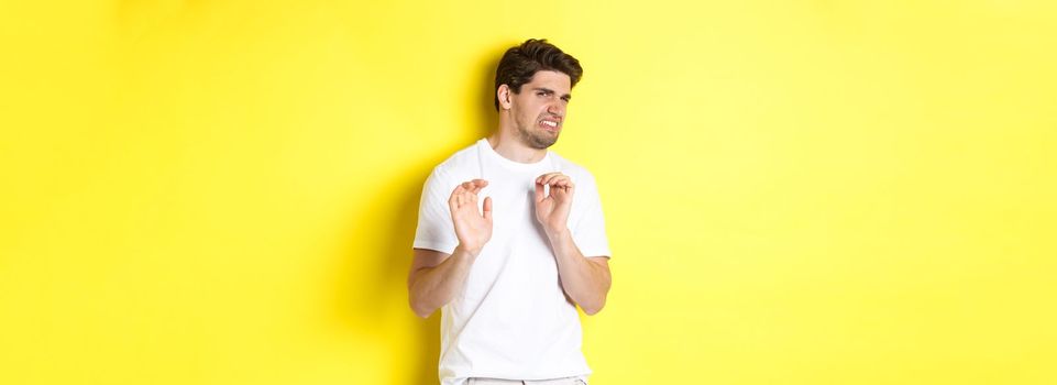 Digusted guy refusing and grimacing, looking at something with aversion, standing over yellow background. Copy space