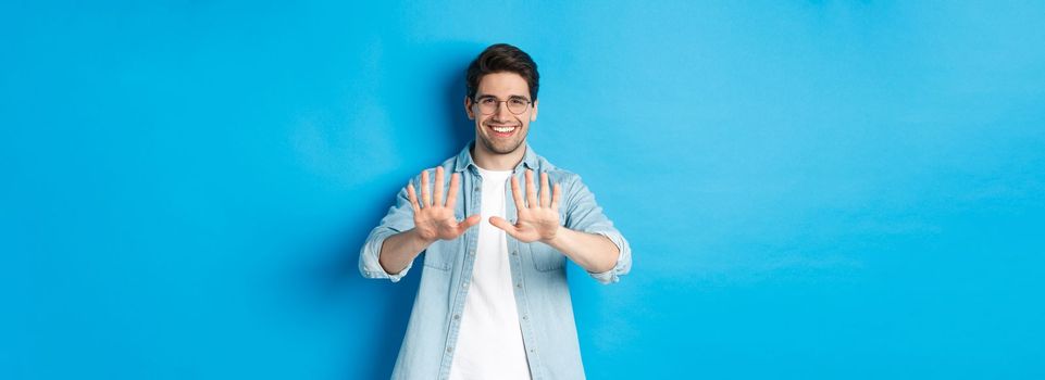 Image of smiling man looking satisfied at his manicure, visit beauty salon, standing over blue background.