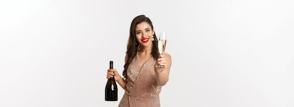 Winter holidays celebration concept. Beautiful woman in elegant dress giving you glass of champagne on Christmas party, standing over white background.