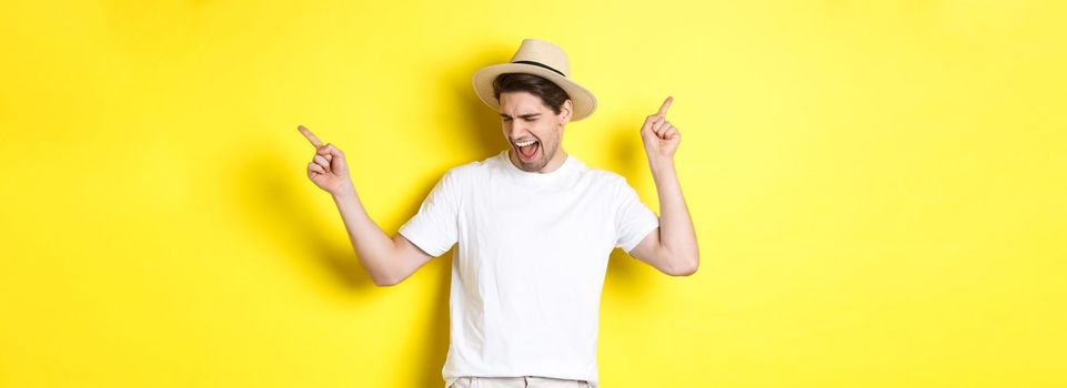 Concept of tourism and lifestyle. Happy man enjoying vacation, tourist dancing over yellow background.