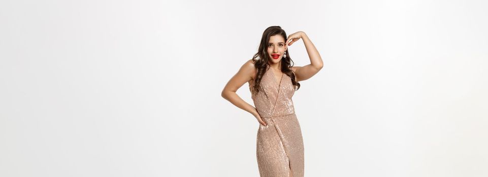 Party and celebration concept. Full-length of glamour woman posing near Christmas presents, wearing evening dress, standing over white background.