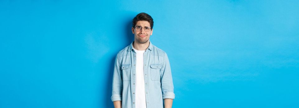 Skeptical and doubtful guy in glasses, looking confused at something strange, blue background.