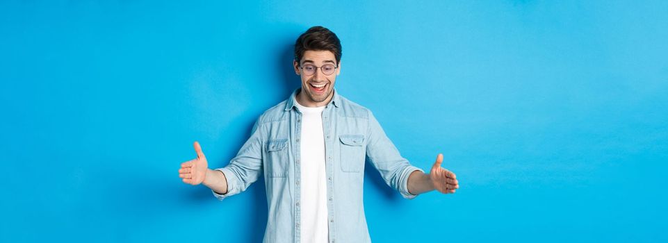 Excited handsome man showing big size object and looking amazed, standing over blue background.