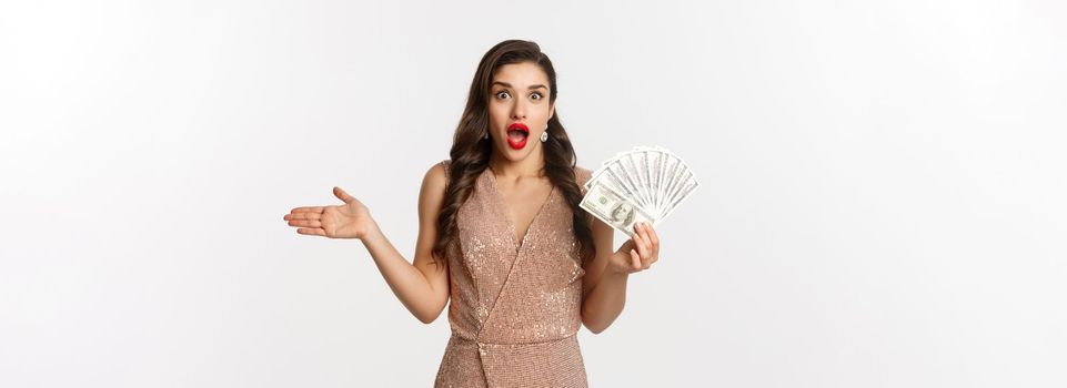 Shopping concept. Elegant woman in glamour dress holding money and looking surprised. winning prize, standing over white background.