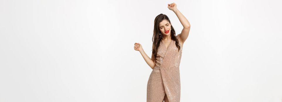 Christmas party and celebration concept. Full-length of attractive woman dancing in luxury dress, having fun, standing over white background.