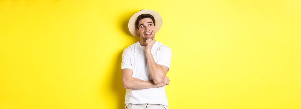 Young thoughtful man tourist imaging something, looking at upper left corner and smiling, thinking and standing over yellow background.