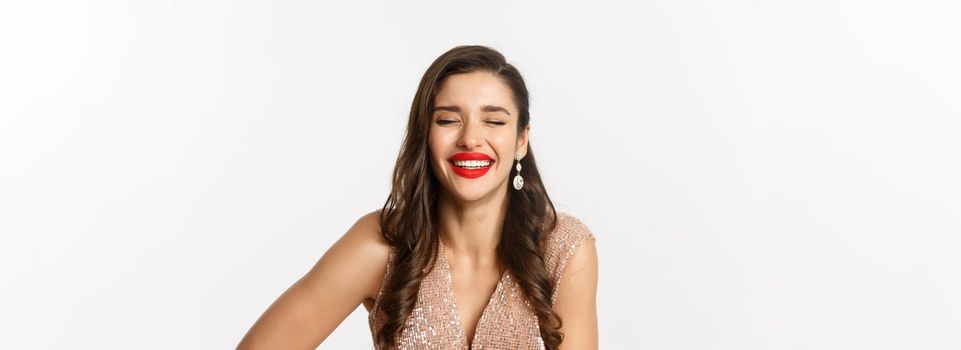 Concept of New Year celebration and winter holidays. Close-up of elegant woman in dress, with red lips, laughing and looking happy, standing over white background.