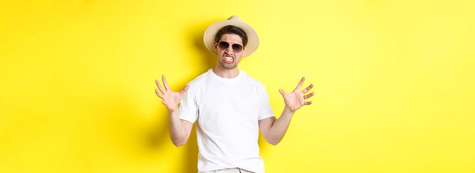 Tourism, travelling and holidays concept. Sassy young man on vacation, showing something big and clenching teeth, standing in sunglasses and summer hat.