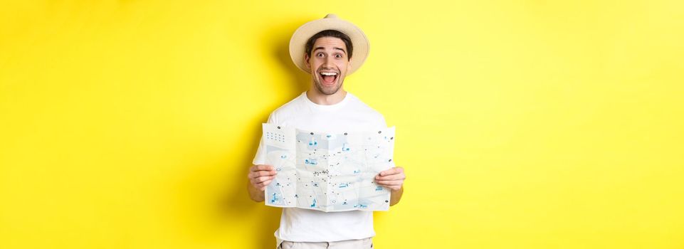 Travelling, vacation and tourism concept. Excited man tourist going sightseeing with map, standing over yellow background.