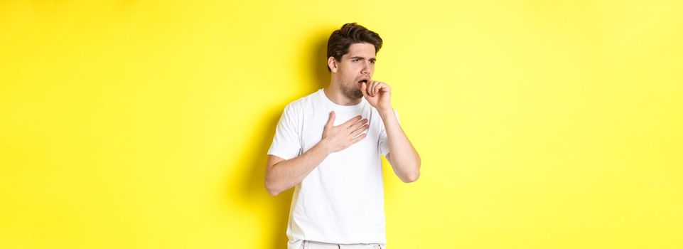 Image of man with covid-19 or flu symptoms, coughing and feeling sick, standing over yellow background. Copy space