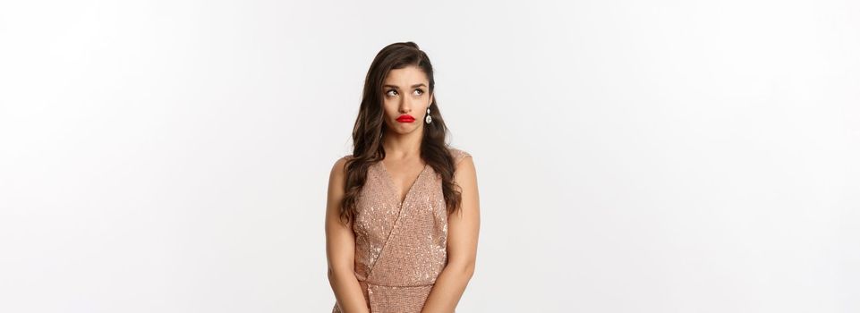 Celebration and party concept. Annoyed young woman losing temper, standing in glamour dress and looking away with bothered face, standing over white background.