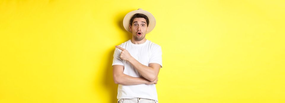 Surprised man in straw hat pointing finger right, showing promo banner, standing over yellow background. Copy space