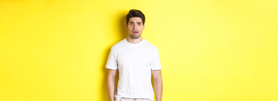 Image of confused and nervous man looking at something strange, frowning anxious, standing against yellow background.