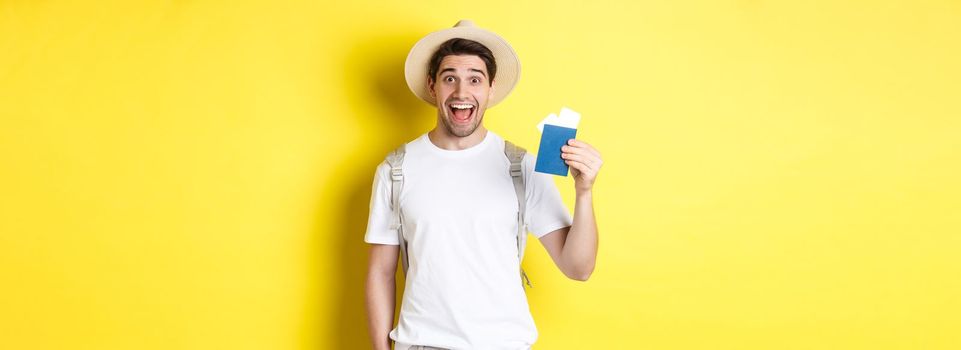 Tourism and vacation. Happy man tourist showing his passport with tickets, going on journey, standing over yellow background with backpack.